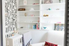 a tiny neutral nursery with a bunny accent wall, built-in shelves, a white crib and a rocker plus some bright textiles