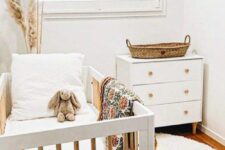 a tiny neutral nursery with a white crib and a dresser that is a changing table, pampas grass, layered rugs