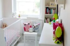 a tiny neutral nursery with white furniture, a built-in bookshelf and a dresser, a banner, some bright textiles and colorful toys