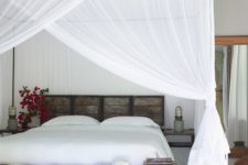 a tropical bedroom with a pallet bed and bench plus mosquito net canopies and curtains