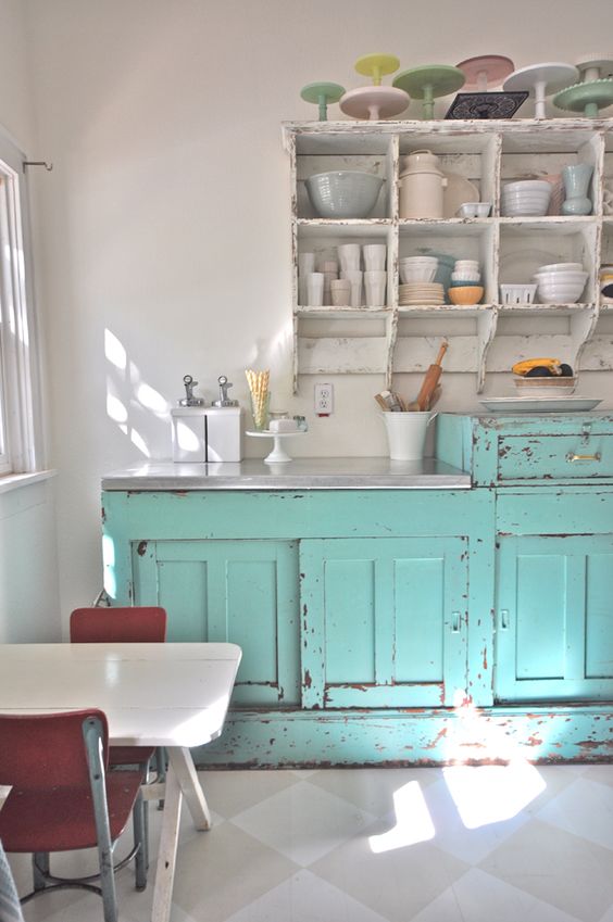 a vintage kitchen with shabby light blue and white furniture, a small dining set and pastel porcelain on top the cabinets