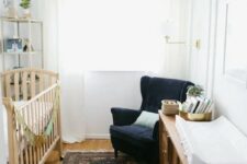 a white nursery is filled with a navy velvet chair, a printed rug and a brown wooden dresser