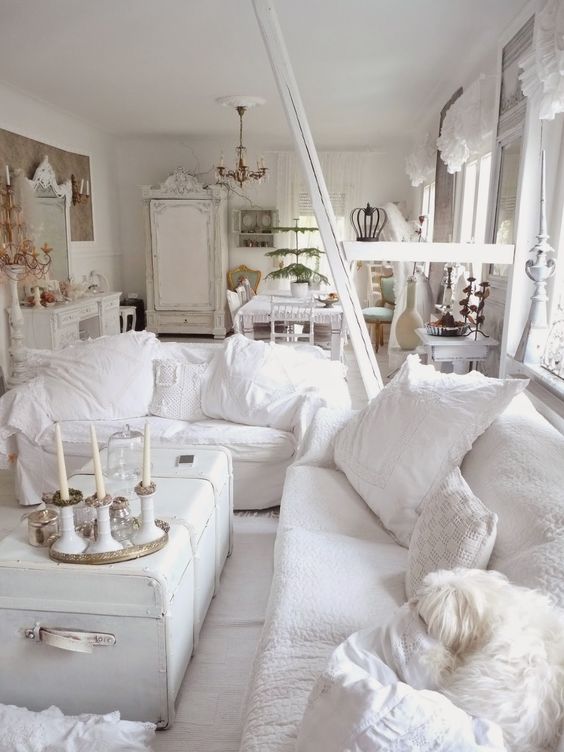 a white shabby chic living room with chic furniture, a white chest, white pillows and candles is very elegant