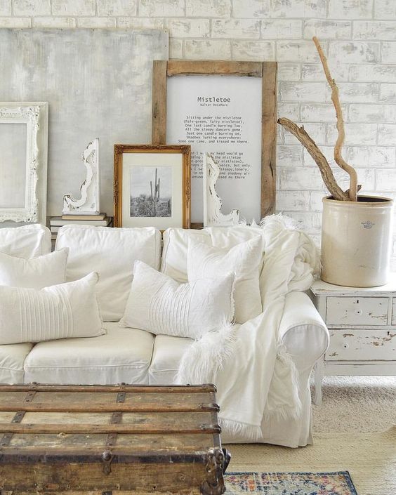 a white shabby chic living space with a gallery wall, a white sofa, a shabby sideboard and a wooden chest