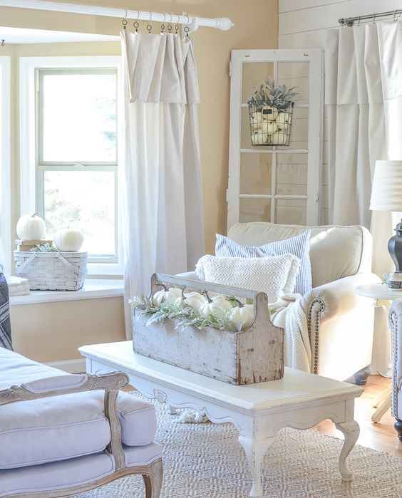 a white shabby chic space with elegant furniture, a low table, a toolbox with blooms and white pumpkins