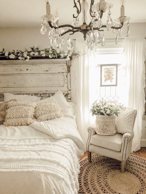 an airy white shabby chic bedroom with a shabby headboard, vintage furniture, a crystal chandelier and neutral blooms