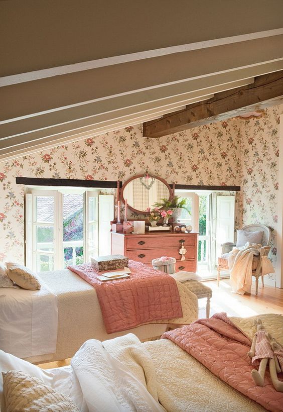 an attic shared kids' bedroom with floral wallpaper, wooden beams, vintage furniture, pink bedding and a dresser and a pink framed mirror