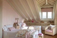 an attic shared shabby chic kids’ room with a pink striped wall, neutral furniture, pink floral textiles and a curtain is very cozy
