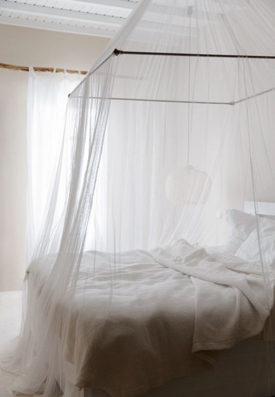 an ethereal white bedroom with a mosquito net canopy over the bed that gives a summer feel to the space