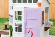 an ice cream inspired kids’ playhouse with a lilac door, a colorful pompom garland, a cactus and a stained dining set behind it