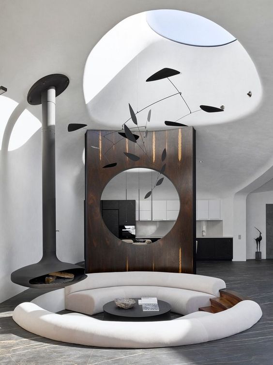 An ultra minimalist and bold round conversation pit with white curved sofas, a black table and a suspended black fireplace