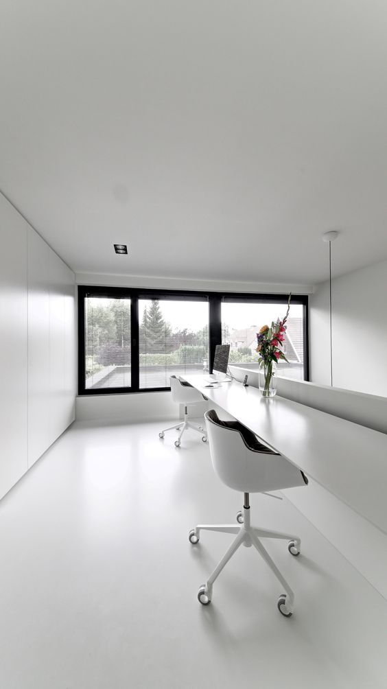 An ultra minimalist home office in black and white, with a floor to ceiling window, a floating shared desk and black and white chairs