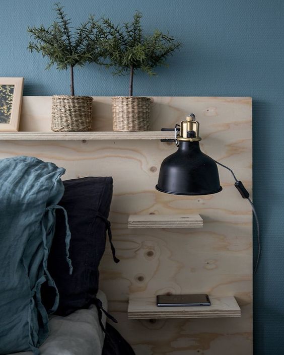 a Nordic bedroom with a blue accent wall, a bed with a storage headboard, potted plants, a large black IKEA Ranarp sconce on the headboard