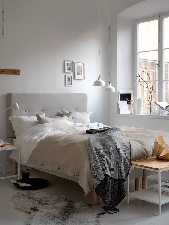 a Nordic bedroom with simple and laconic furniture, a grey upholstered bed, white pendant lamps over the space