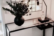a Nordic space with a black Vittsjo table, a black vase with euclayptus and thistles, a table lamp and grids with photos over the table
