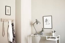 a Nordic space with a white Vittsjo desk, a creamy chair, a grey lamp and some pen jars and a black and white artwork