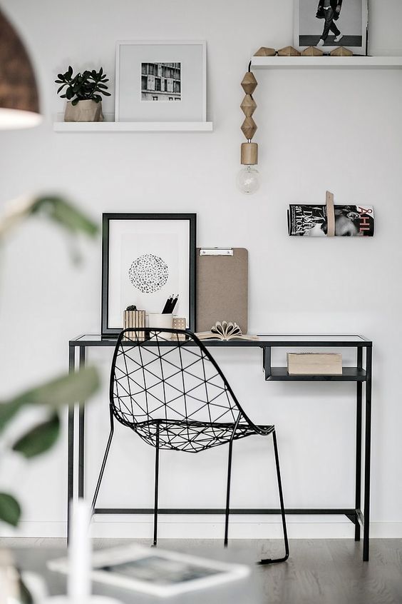 a Nordic working space with a black Vittsjo table and a black metal chair, open shelves with artworks and potted plants and some books