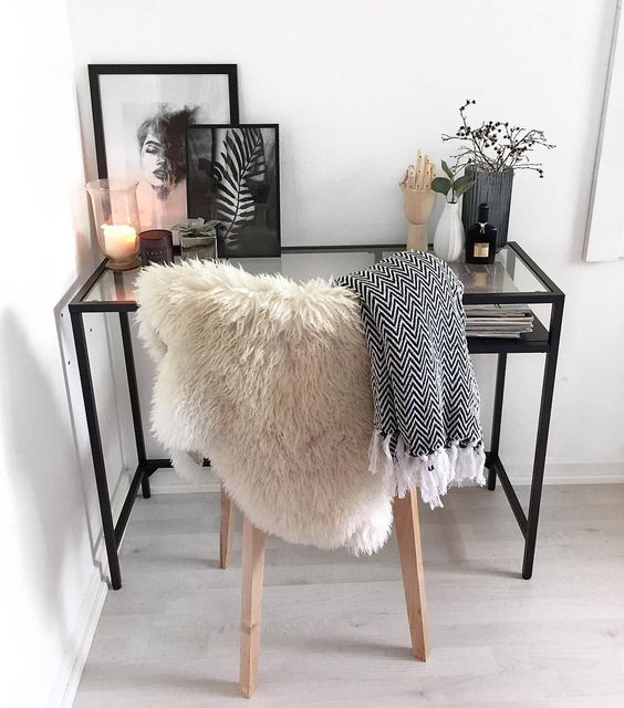A Scandinavian working space with a black Vittsjo desk, a light stained chair, some candles and greenery and black and white artworks