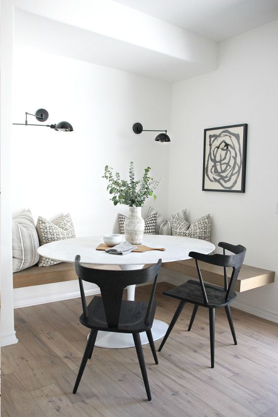 a beautiful Scandinavian dining space with a floating bench, a round table, black chairs, black sconces and a graphic art