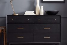 a black IKEA Malm dresser with brass handles and little knobs on tall legs is a chic mid-century modern piece of furniture