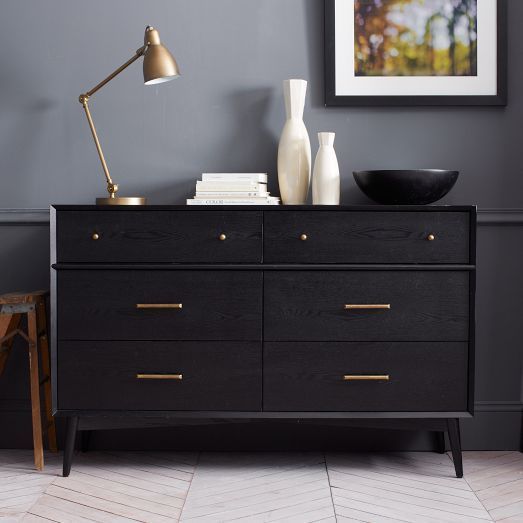 A black IKEA Malm dresser with brass handles and little knobs on tall legs is a chic mid century modern piece of furniture