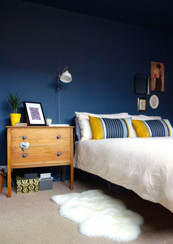 a bold bedroom with navy walls, stylish mid-century modern furniture, white IKEA Ranarp wall sconces