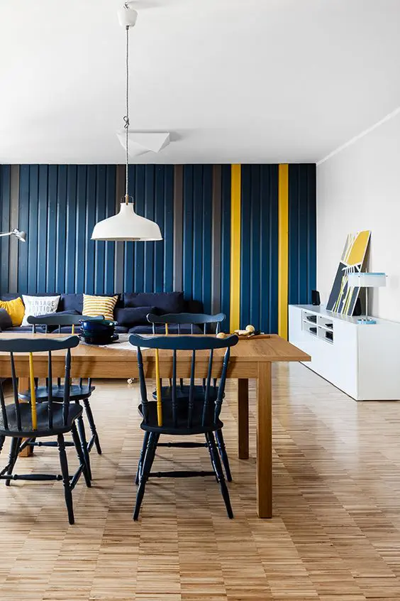 a bold navy and yellow open layout for a living and dining room, white pendant IKEA Ranarp lamps over the dining space