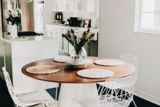 a chic modern dining space with a round table, metal chairs, a jute rug, a modern chandelier and some blooms