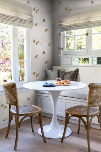 A cool and cozy dining area with a built in bench, a round table, woven chairs, beautiful wallpaper and views