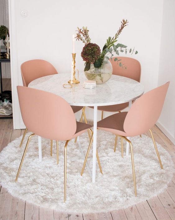 a cozy glam dining nook with a round table, pink chairs, a vase with blooms and a candle plus a fluffy rug is very cool
