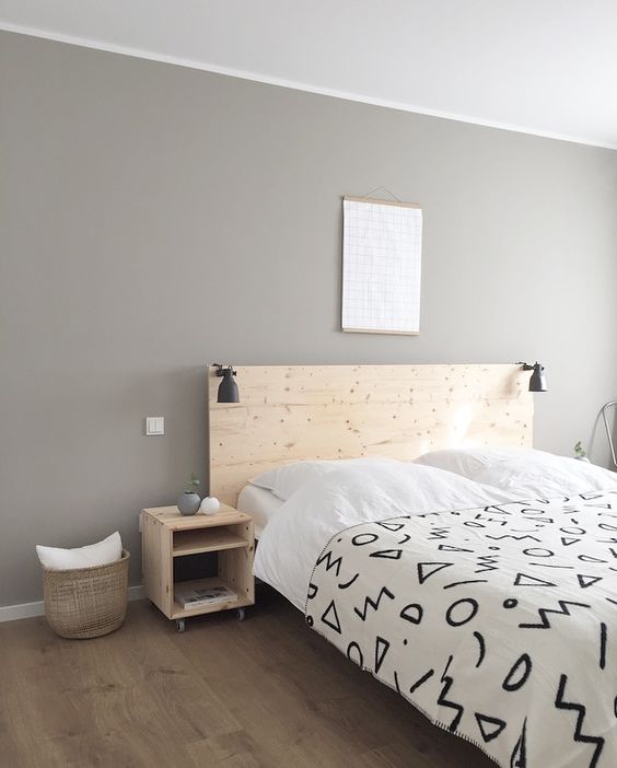 A laconic minimalist bedroom with light colored wooden furniture, a basket, artworks and black IKEA Ranarp sconces