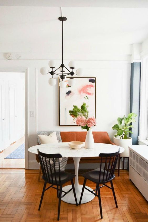 A lovely modern dining area with a rust colored leather loveseat, printed textiles, a round table, black chairs, a modern chandelier