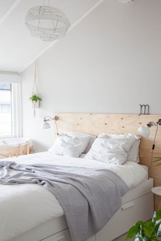 a neutral Nordic bedroom with a white bed with storage, a plywood headboard, IKEA Ranarp sconces that brign light