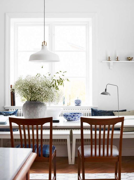 a peaceful dining space with simple and elegant furniture, greenery, chic porcelain and a white pendant IKEA Ranarp lamp