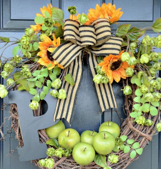 a rustic fall wreath of vine, foliage, greenery, bright blooms, apples, a striped bow and a large monogram