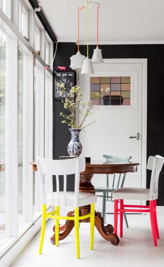 a small and colorful dining space with a vintage dark stained round table, chairs with colorful legs, pendant lamps on colorful cords