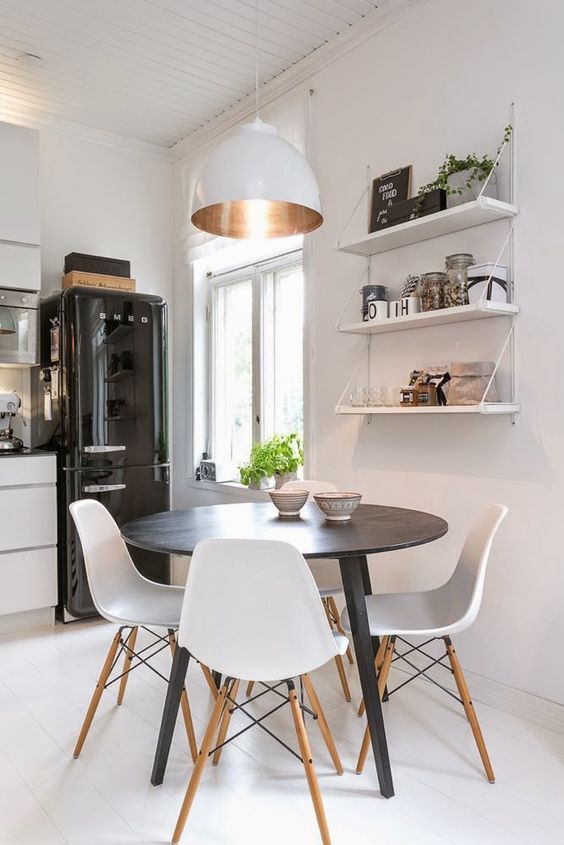 a small and cozy dining nook with open shelves, a round table, white chairs, a chic white pendant lamp