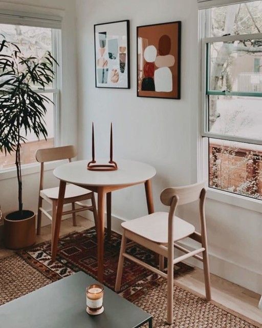 a small modern dining nook with a round table, wooden chairs, a pretty gallery wall, a potted plant and layered rugs
