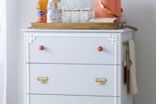 a whimsy IKEa Tarva hack in dove grey, with brass and red knobs plus white inlays and casters makes up a cool home bar