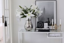 an elegant Scandinavian entryway with a white Vittsjo table as a console table, a black and white artwork, blooms, candles and books
