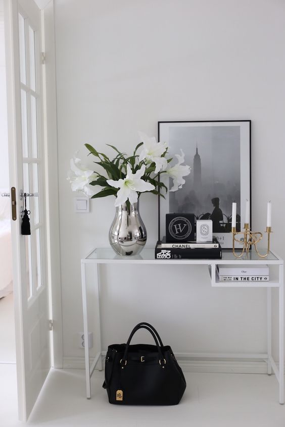 an elegant Scandinavian entryway with a white Vittsjo table as a console table, a black and white artwork, blooms, candles and books