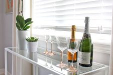an elegant console table and home bar of a white Vittsjo desk, potted plants and blooms, elegant glasses and wine and champagne bottles