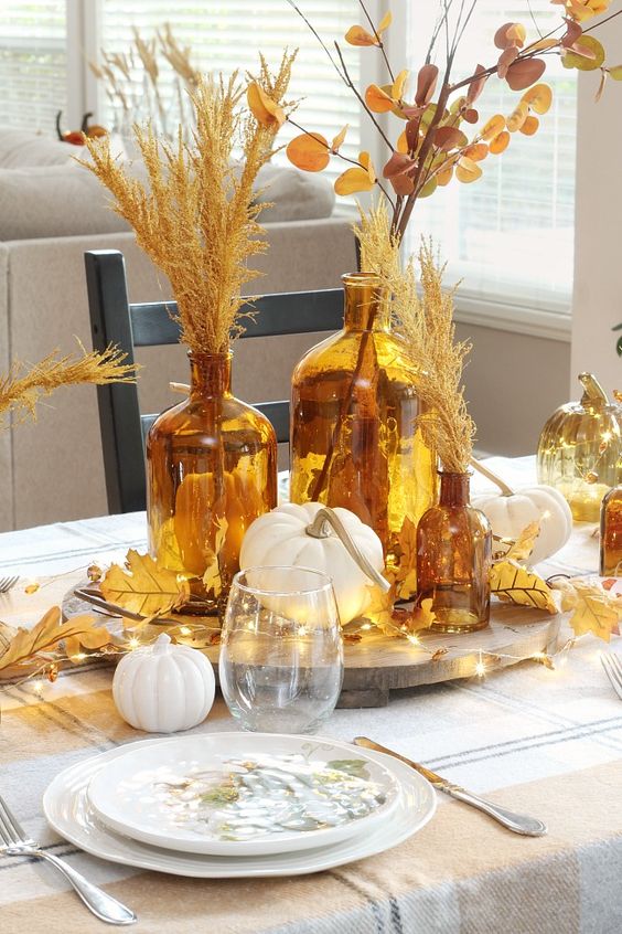 a beautiful rust and gold centerpiece of pumpkins, apothecary bottles with grasses and leaves and lights