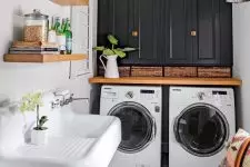 a bold modern laundry with a marble tile floor, black cabinets, a wooden countertop and a washing machine and a dryer, a sink and a basket