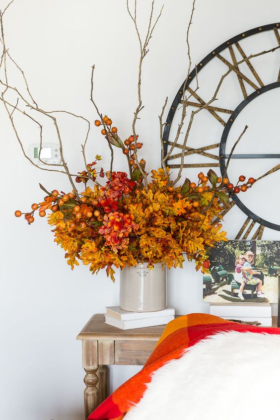 a bright and fun fall centerpiece of orange leaves, red blooms, branches with berries is a stylish idea