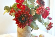 a bright fall centerpiece of red and burgundy blooms, greenery in a vintage jug is a bold decoration
