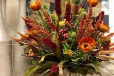 a bright rustic arrangement of rust, burgundy faux blooms, dried herbs and greenery and wooden sticks in the vase
