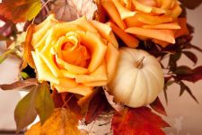 a bright rustic fall centerpiece of orange roses, fall leaves, a white pumpkin and a vase wrapped white bark