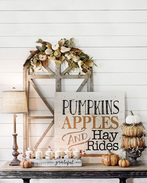 A chic whitewashed wooden sign with black and rust colored letters, pumpkins and candles around
