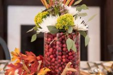 a chic woodland fall centerpiece of a wood slice, antlers, fall leaves, a glass with cranberries, blooms and leaves